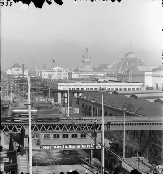 Elevated view of buildings at the Columbian Exposition in Jackson Park, viewed from Stony Island Avenue. The "L" station and train are in the foreground. Sign at station reads: "Stony Island Ave. Station 'Alley L' to City."