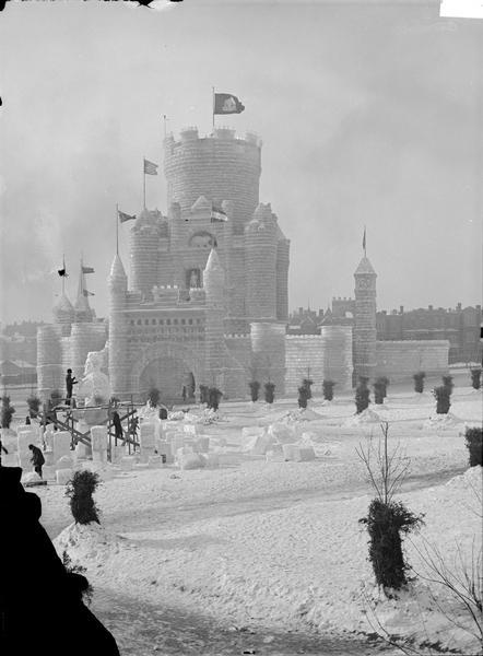 The ice palace at the St. Paul Ice Carnival. People are on and around a scaffold in the left foreground carving busts out of ice. Blocks of ice are on the ground around the scaffold.