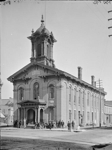 A group of men sitting and standing in front of Old City Hall (built 1860).