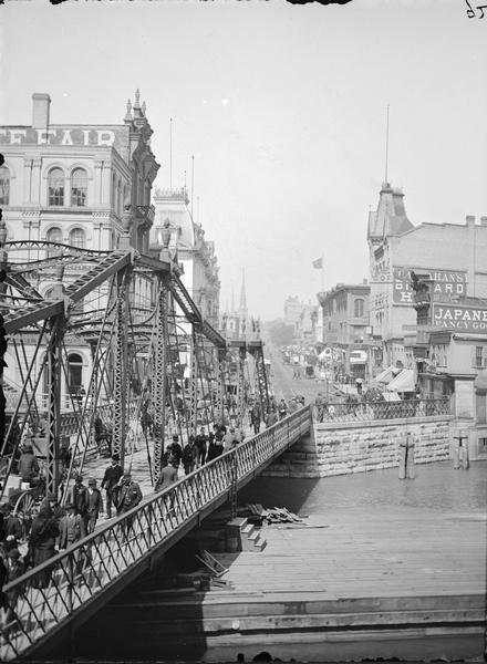 View up Grand Avenue from bridge. Pedestrians and horse-drawn vehicles cross bridge on the left.