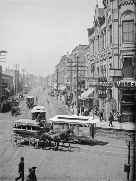 Elevated view of buildings and traffic on West Water Street, with horse-drawn vehicles and streetcars in foreground.