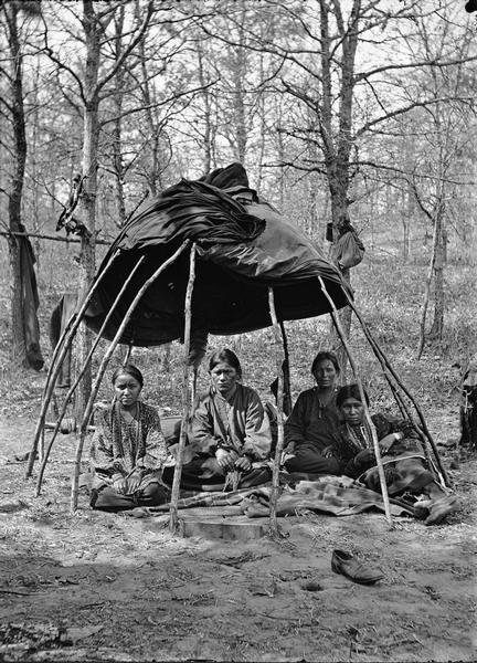"Indian Tent and Ho-Chunk Women."  Four Ho-Chunk women are sitting under a basic traditional structure (chipoteke).