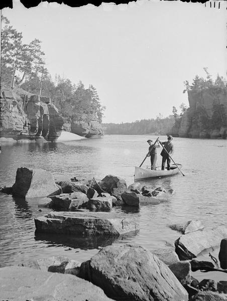Looking downstream through the Jaws. Two men are standing in a canoe, each holding an oar.