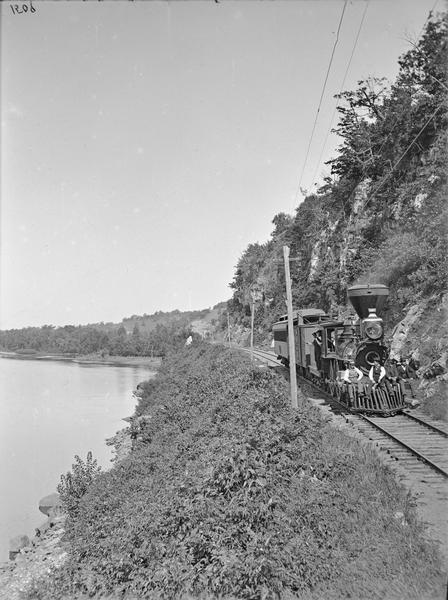 Upper Mississippi, Minnesota, near Hastings. Engine and car of the Chicago, Milwaukee and St. Paul Railway with men posing sitting on the cattle-catcher, leaning out of engine cabin.