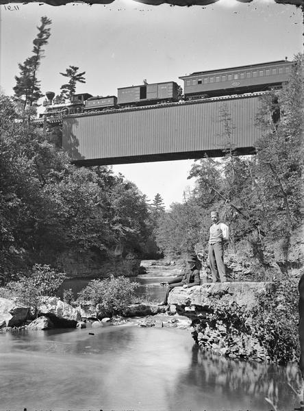 Upper Mississippi; The Chicago, Milwaukee and St. Paul railroad bridge across the Vermillion River. A CM&SP train is crossing the bridge. Two men are posing on a rock in the foreground, one sitting, one standing.