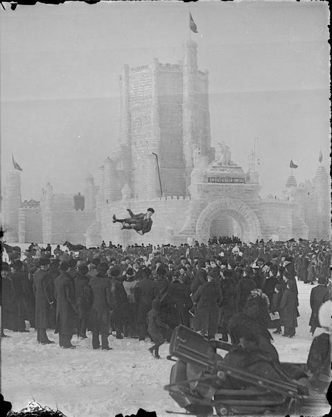 St. Paul Ice Carnival. A man being bounced is suspended in the air above a crowd of people. In the background is an ice castle. In the foreground is a horse-drawn vehicle.