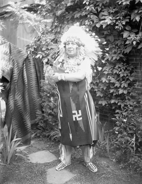 Full-length outdoor portrait of Oscar Norton, also known as "Chief Silver Tongue."  There is a brick wall, foliage, and blankets in the background.
