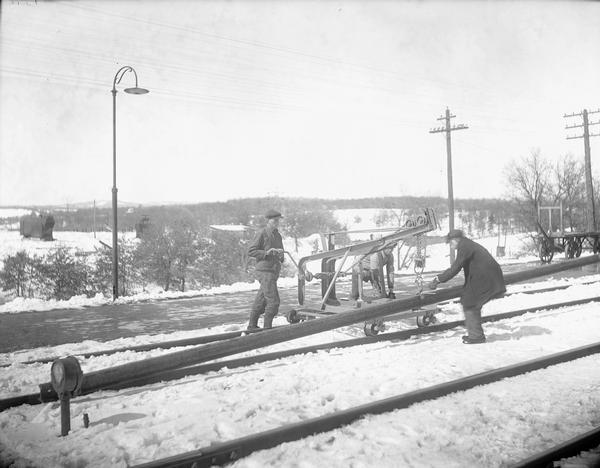Three men are laying rail on snow-covered ground at the Kilbourn railroad station.