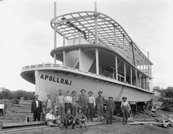 Group portrait of men posing in front of the partially constructed "Apollo No. 1" steamboat.