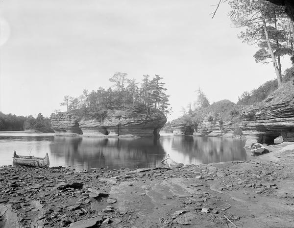 View across river towards Lone Rock. There are canoes on the rocky shoreline in the foreground.