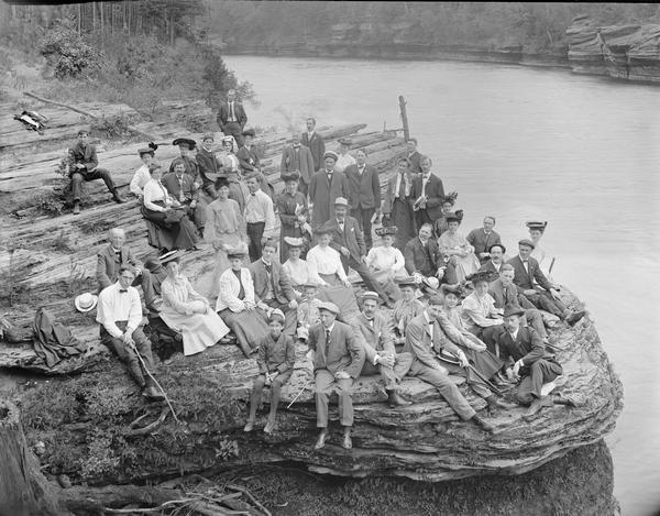 Elevated group portrait of unidentified visitors posing on a rock overlooking the river.