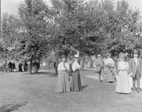 Unidentified group of people walking at Kilbourn railroad park. Trees and buildings are in the background.
