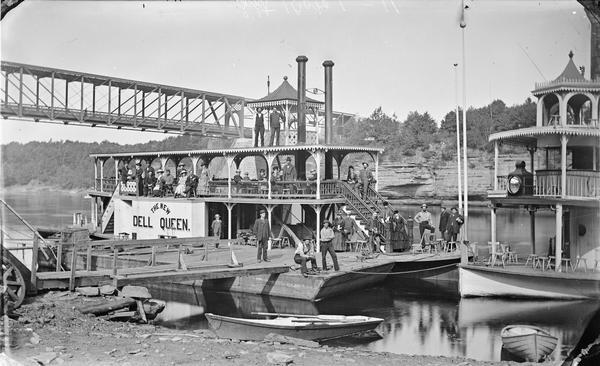 Passengers posing on the "New Dell Queen" steamboat. Bow of second steamboat on right. Bridge in background.