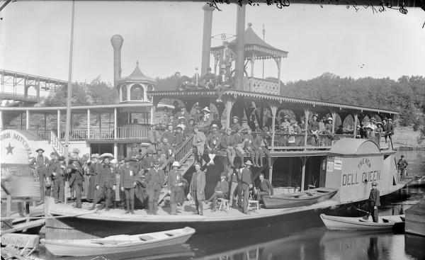 <i>New Dell Queen</i> steamboat and passengers at landing. Steamboat <i>Alexander Mitchell</i> partially visible on left. Bridge in background.
