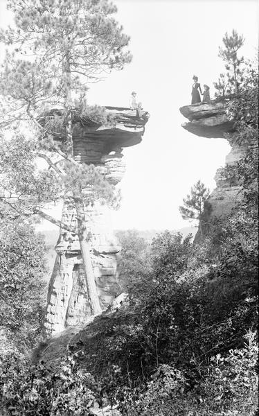 Man sitting on Stand Rock, a woman and child posed standing on opposite rock ledge.