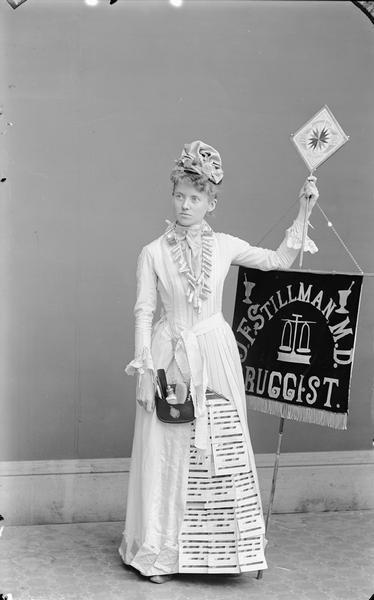 Studio portrait of Mrs. Ed Dixon dressed to advertise druggist J.F. Stillman.