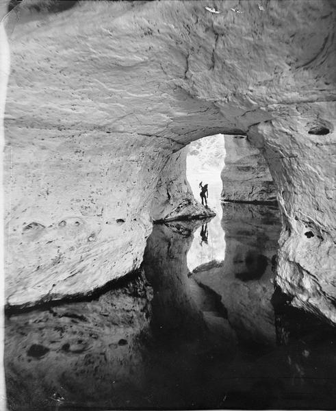 Looking out of the Cave of the Dark Waters through the Reflection Arch. A person dressed as an "Indian" is standing just inside the cave opening, appearing to fish.