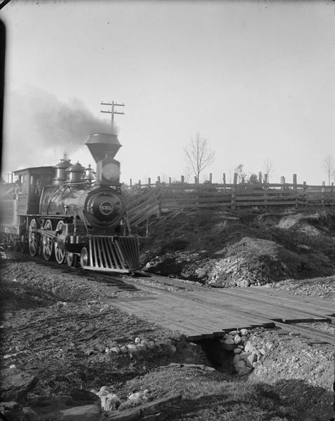 Kilbourn; little wood burner locomotive (train engine) at crossing.