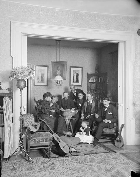 Interior portrait of the Bennett family posing around a bowl of popcorn. They are sitting in an alcove with the pocket doors open, and three stringed instruments are propped against a chair and a wall.