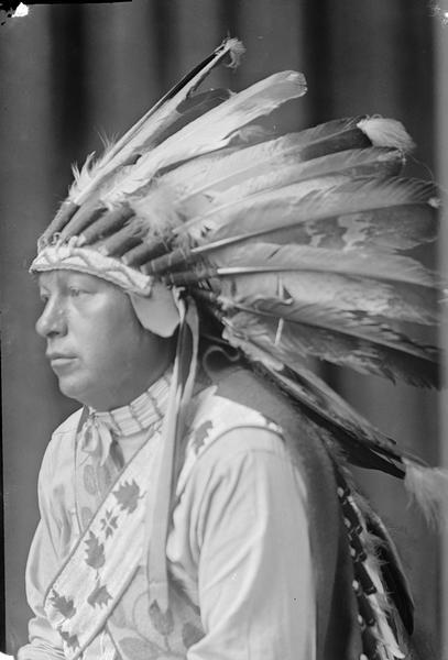 Studio portrait of Ho-Chunk man in profile with eagle feather.