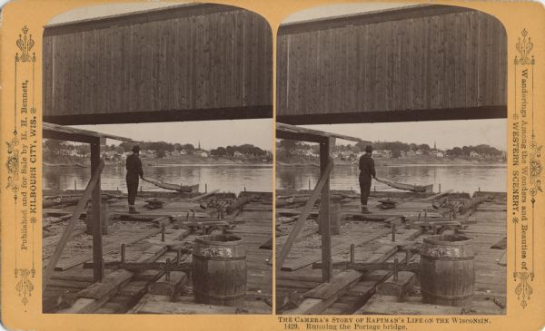 Stereograph of a man standing on the back of a raft holding a hand-hewned oar. The raft is passing under a wooden bridge. A town, including a church, are in the background.