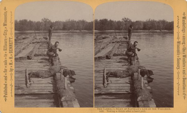 Stereograph of a man lying on his stomach on a raft drinking water from the river. A second man crouches on the edge of the raft while a third man is standing lifting something to his mouth. In the distance is a raft at the shore.