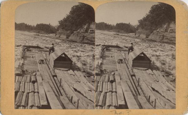 Stereograph of a man on the end of the raft as he prepares to pass through the water's rough rapids.