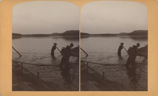 Stereograph of several men working at dusk, knee deep in water attending to the raft.