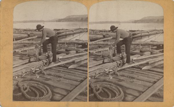 A man tying a rope around a log on a lumber raft.