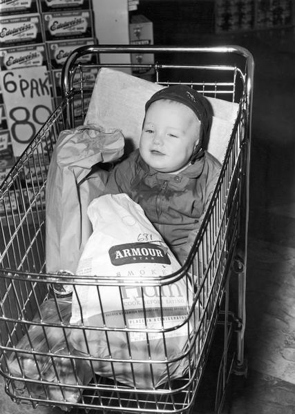 Child in a shopping cart with a frozen Armour smoked ham.