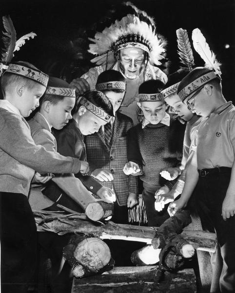 Young Caucasian boys dressed like Native Americans as part of their YMCA "Indian Guides" program. They are being directed by the "All Nations Chief" Henry Boettcher.
