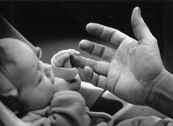 Infant son holds father's finger.