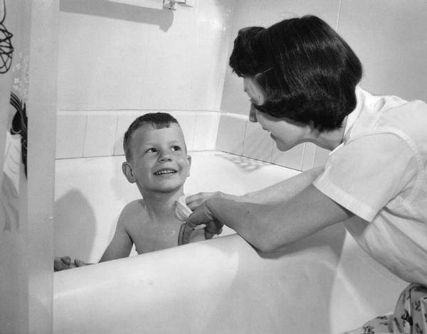 A boy in the bath tub being bathed by his mother.