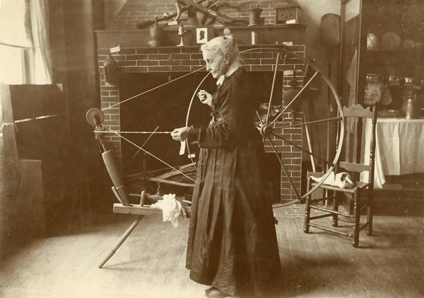 Elderly woman using a spinning wheel to make yarn from wool.