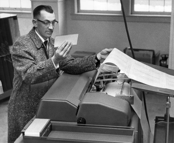 A farmer observes the processed results of the workings of an early computer or data machine. The machine was used to process and to organize data on a herd of cows for farmers.