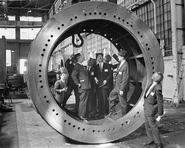 Japanese businessmen visit an American manufacturing firm in South Milwaukee and pose inside a huge metal implement.  The American firm is Bucyrus-Erie and the Japanese firm is Komatsu Manufacturing.