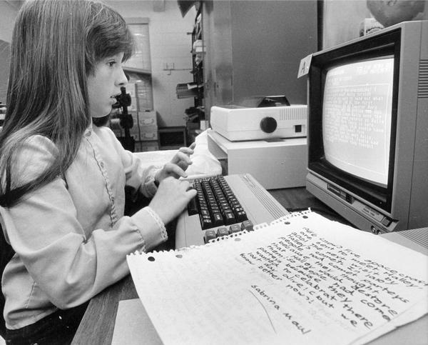 Schoolgirl watches the monitor as she types her story on a word processor.