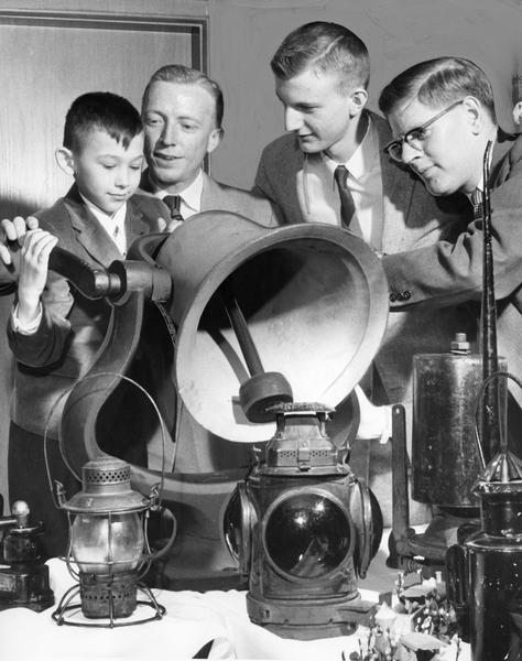 A young boy rings a locomotive bell. Other artifacts of locomotive history are on the table before him with members of the Milwaukee chapter of the National Railway Historical Society.