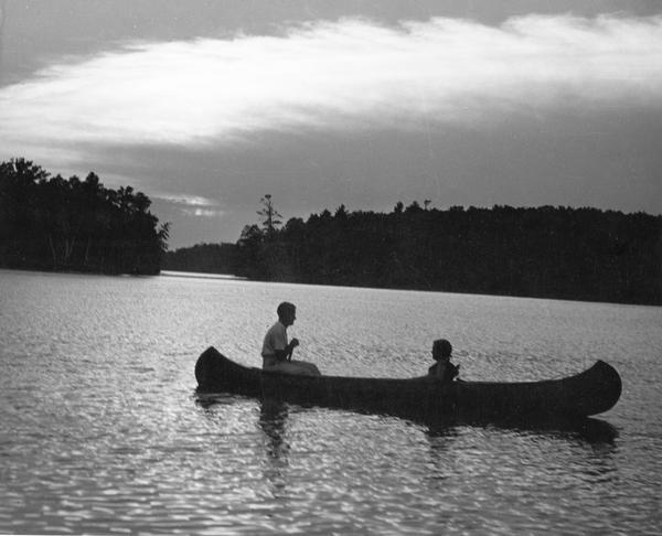 Couple canoeing under partly cloudy skies with sun dappling the water on Rainbow Lake, Chain O' Lakes.