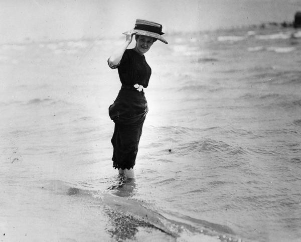 Woman in wide brimmed hat wading in water.