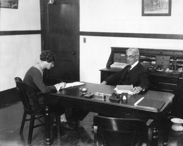 A businessman and his secretary at the desk in his office.