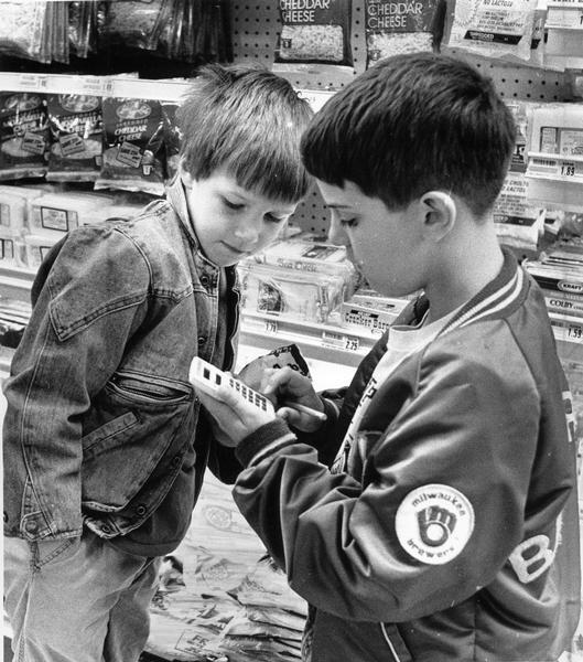 Two young boys in a grocery store figuring out prices of food with a calculator.
