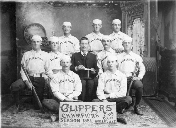 The Neillsville "Clippers" baseball team pose for portrait in front of a painted backdrop.