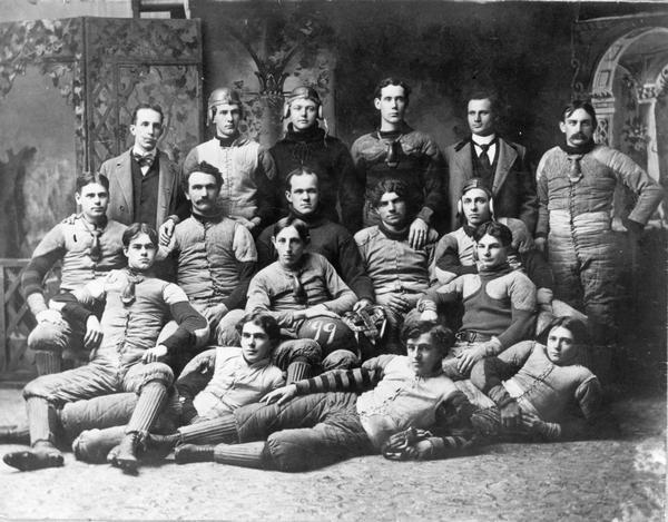 Group portrait in front of a painted backdrop of members of a Whitewater, Wisconsin football team.