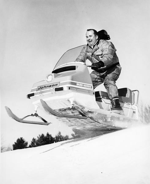 Man jumps off a hill on a "Johnson" snowmobile.