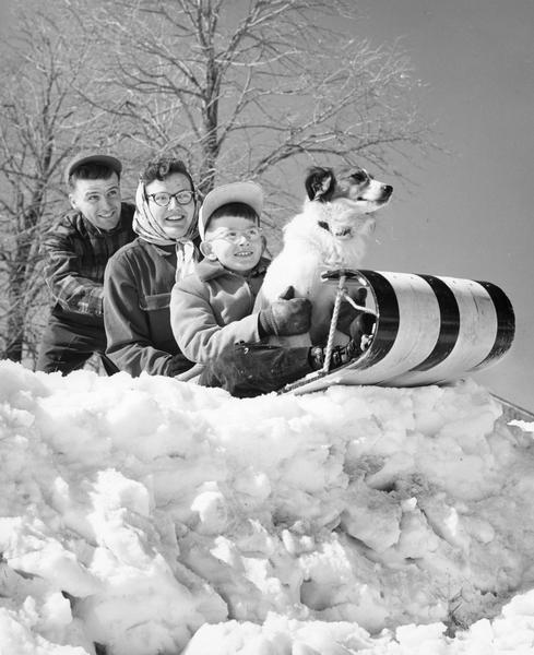 Winter scene with a family and their dog preparing for their descent down the hill on a toboggan. From left to right, Gene Anderson (my uncle), Betsy Marquardt (Anderson)(my aunt), Lynn Anderson(my father, and Spot. It was taken on the Anderson Farm, Maurice and Wena (Rademaker).