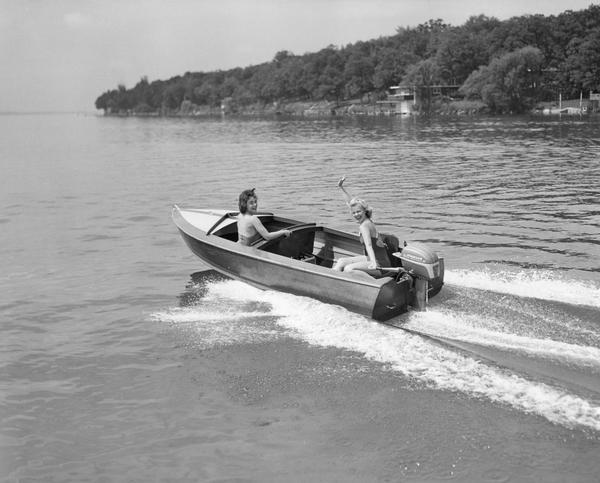 Two women motorboating and waving to the photographer.