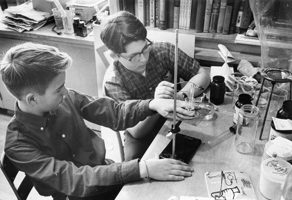 Two young boys work on a science project in a lab room.