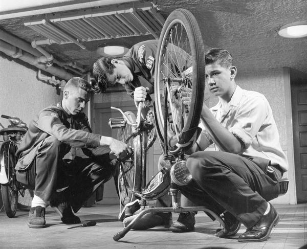Three young men repair a bicycle.