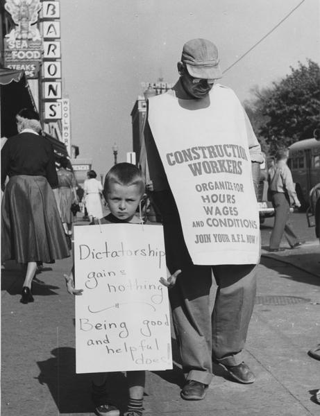 A young child, Frank Hill, walking the picket line at a strike with an older man. The adult's sign reads: "Construction Workers organize for hours, wages and conditions - Join your AFL now."